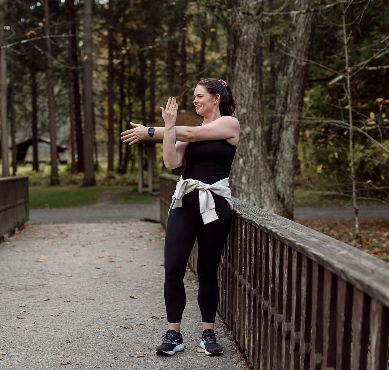 Emily stretching her shoulder on a wooden bridge in a park